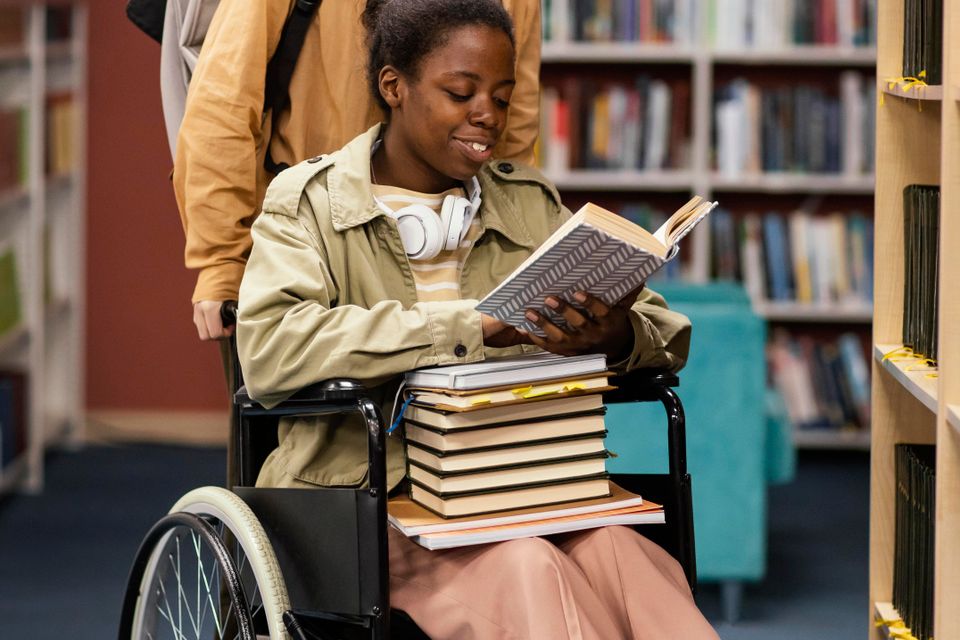 Girl helping her colleague wheelchair choose book project