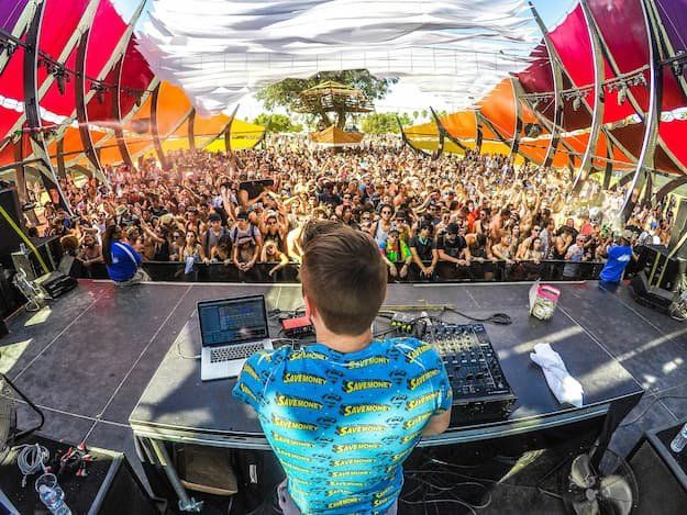 A DJ taken from the perspective of the DJ with a crowd dancing and cheering in front of them
