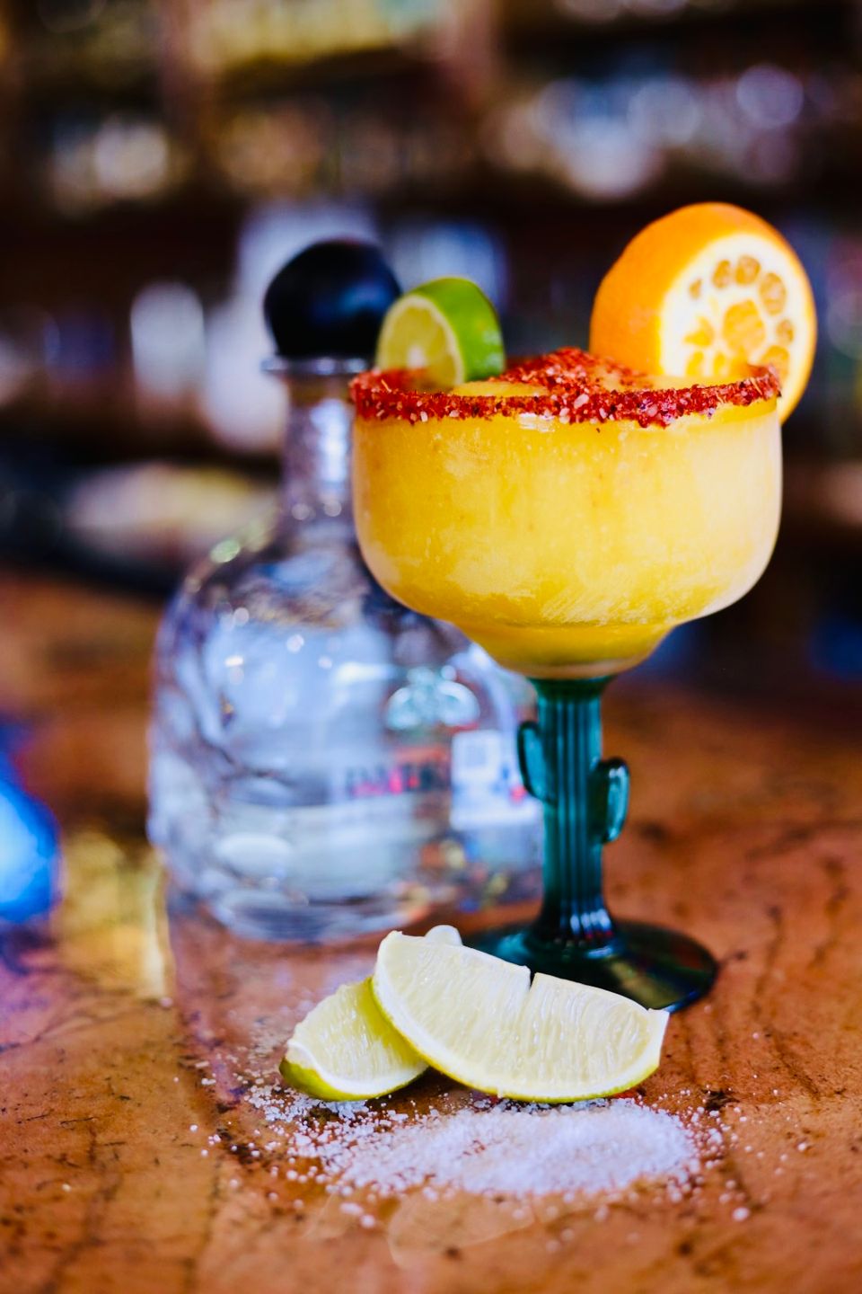 Mango Margarita with Tajin on rim, Bottle of Patrón Tequila behind it and wedges of lime and salt on the bottom.