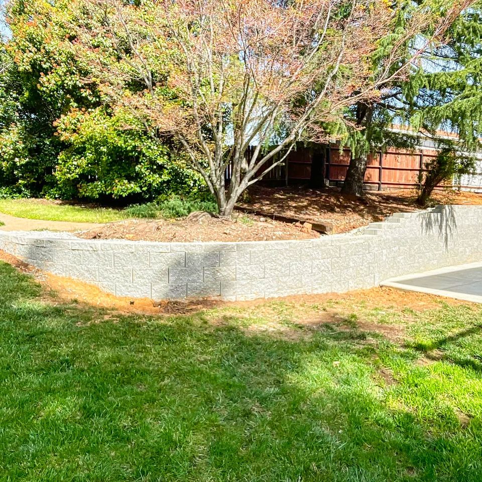 Completed luxury backyard remodel by Alta Vista Landscaping & Tree Service featuring a custom stacked stone fire pit, stamped concrete patio, and a tiered block retaining wall with integrated seating in El Dorado County