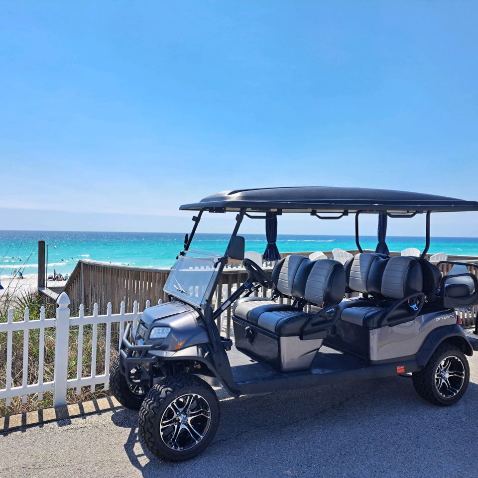 Gray six-passenger golf cart rental parked at a beach access boardwalk overlooking turquoise water in Destin Florida