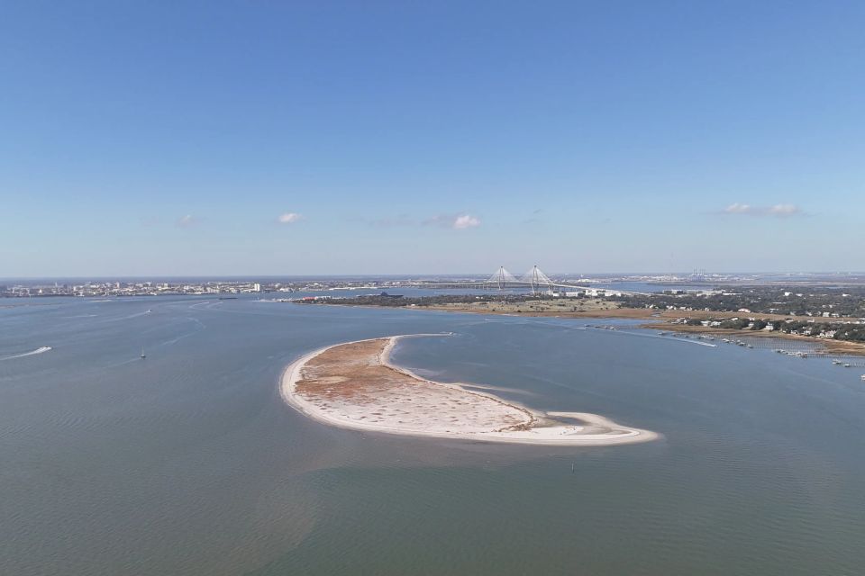 Aerial view of Crab Bank Island’s crescent sandbar in Charleston Harbor, with the Arthur Ravenel Jr. Bridge and Mount Pleasant skyline in the distance
