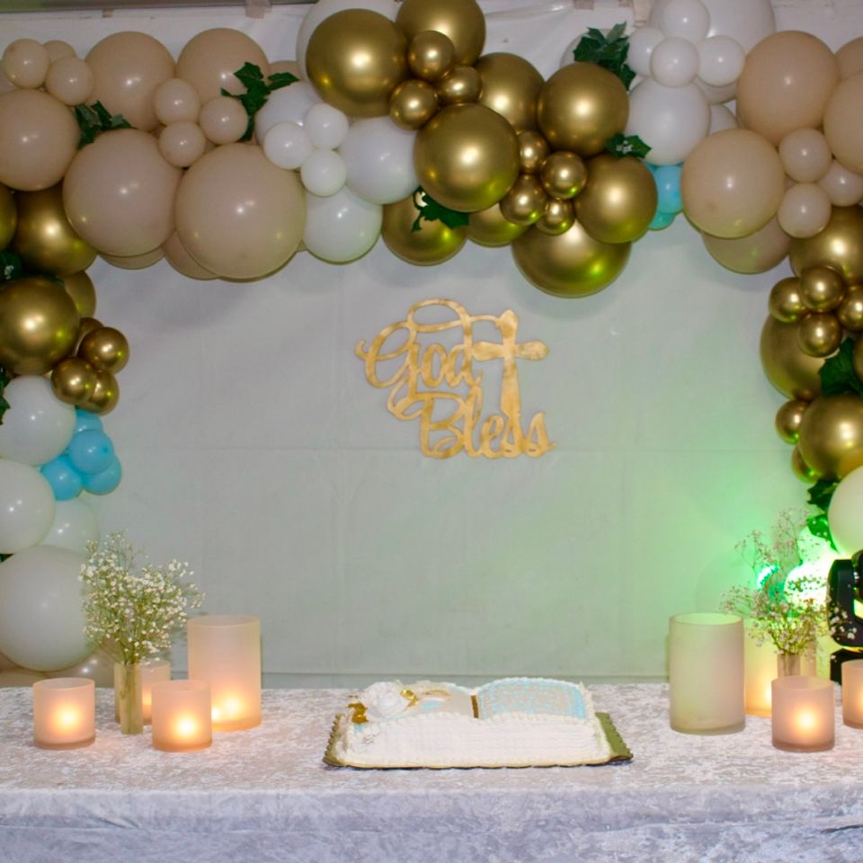 Gold and ivory balloon garland backdrop framing a cake table with candles at a celebration