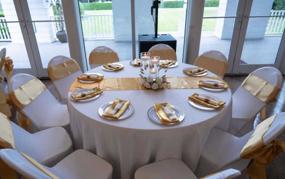 Round banquet table styled with gold sashes, satin napkins, and floating candle centerpiece