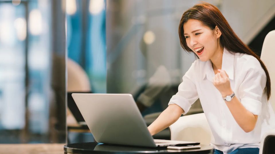 Young woman celebrating something she's seeing on her laptop monitor.