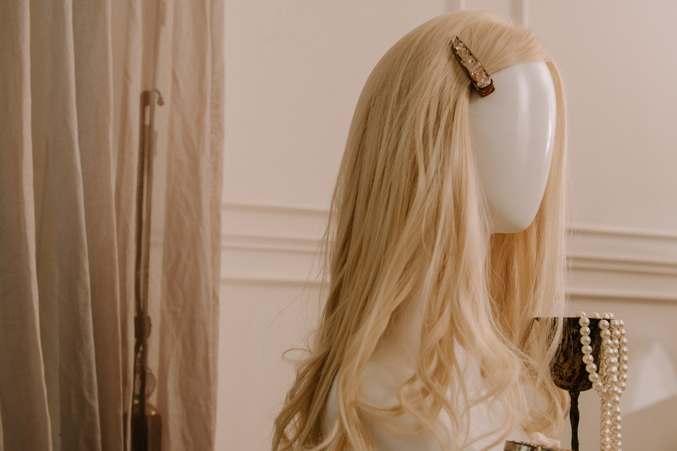 Long blonde wig displayed on a mannequin with soft layers, loose waves, and a side hair clip at Shears Wigs & Hairpieces Salon.