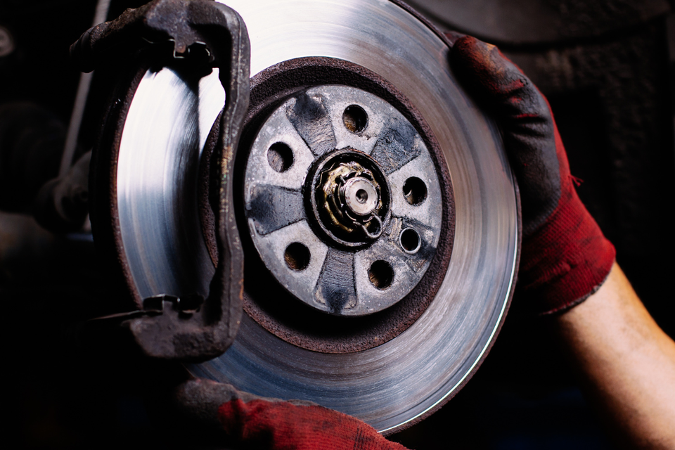 Technician servicing a vehicle brake rotor and brake pad during a brake repair service.