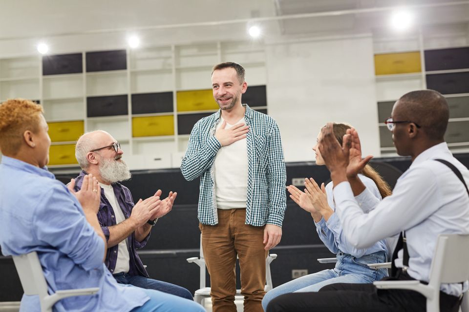 Portrait of smiling mature man introducing himself during therapy session in support group to people clapping copy space stockpack gettyimages scaled