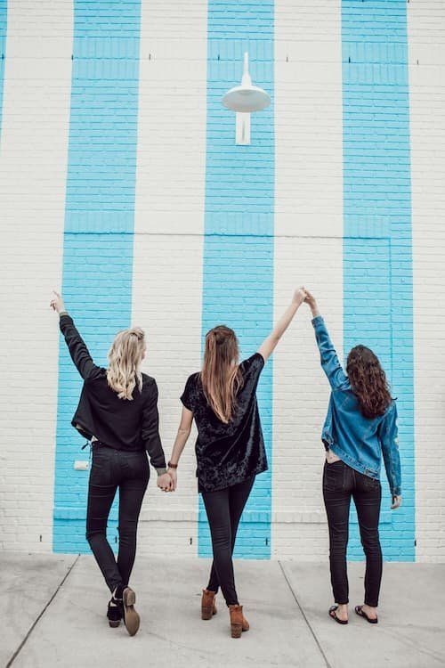 Three women holding hands celebrating with their backs to the camera 