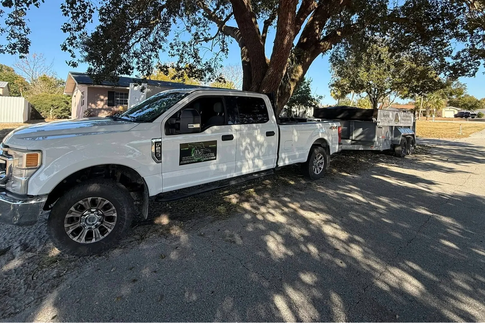 JNJ Hauling Solutions white pickup truck under a tree
