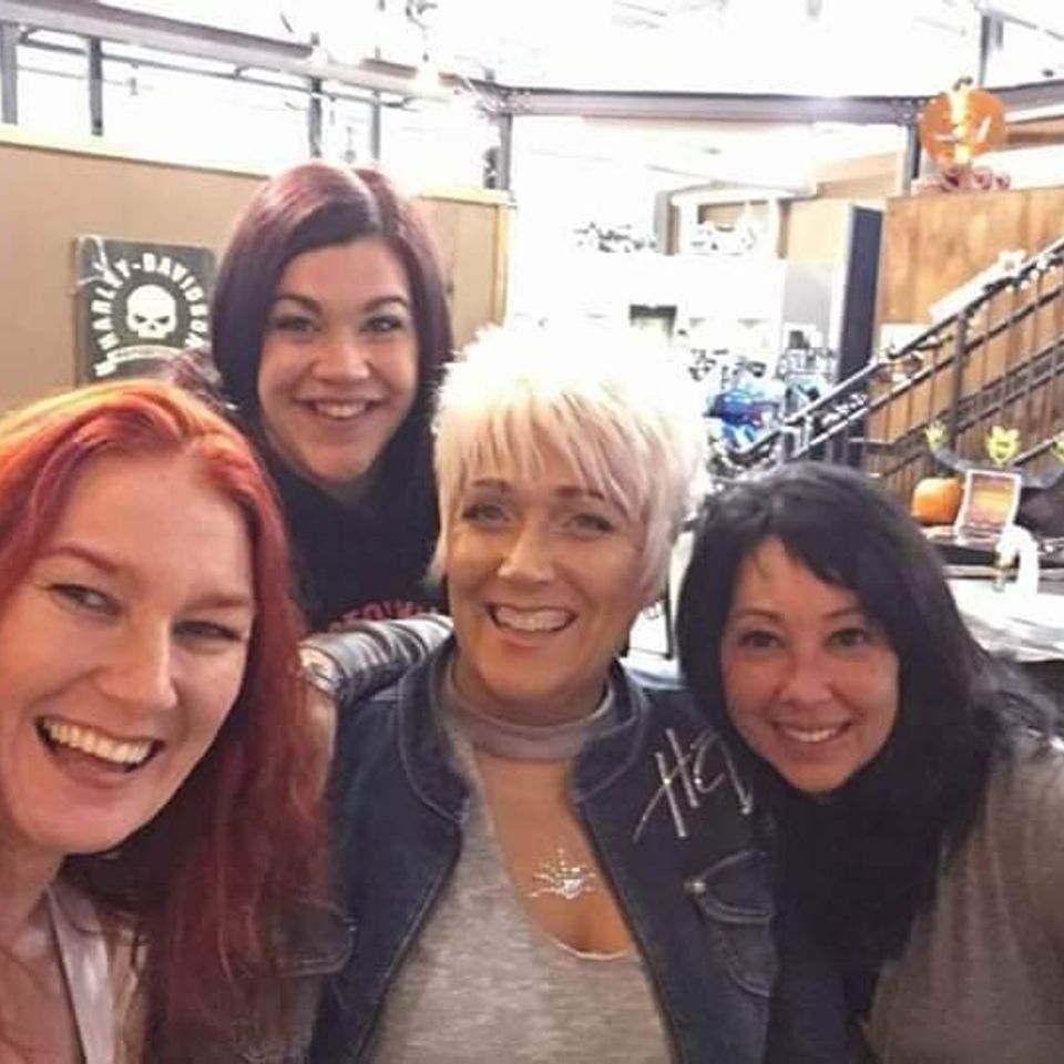 Four women posing together inside a venue during a casual social event.