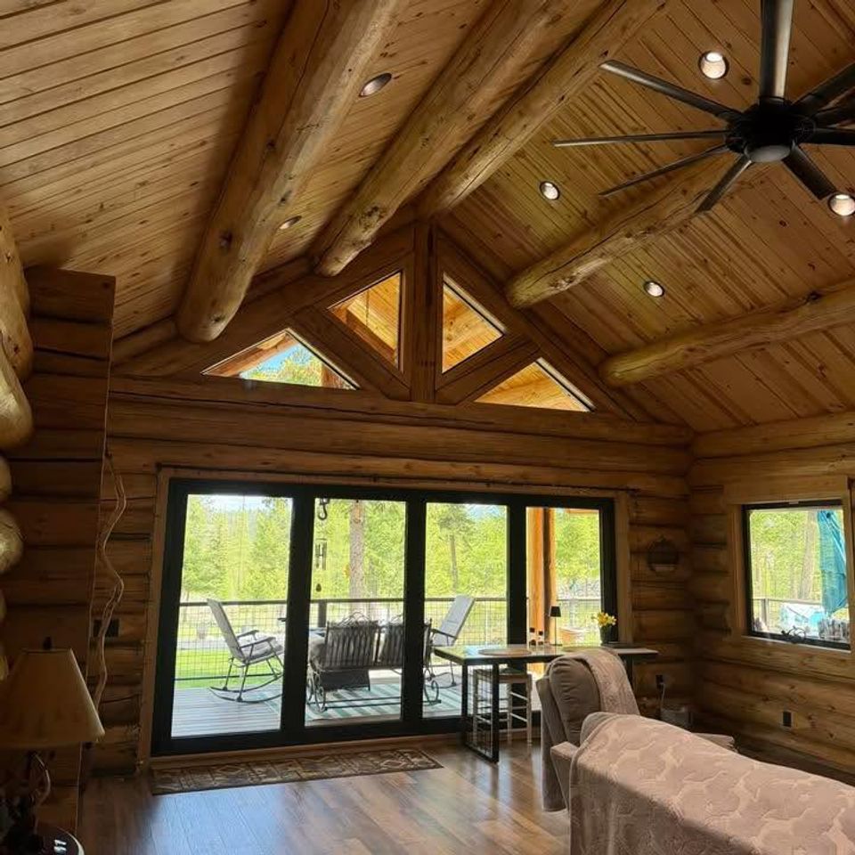 Log home living room with exposed round log beams and sliding doors to a covered deck in Trout Creek