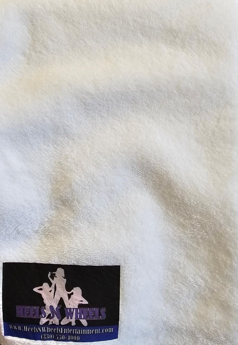 Close-up of a white towel displaying the Heels 'n Wheels logo and website information.