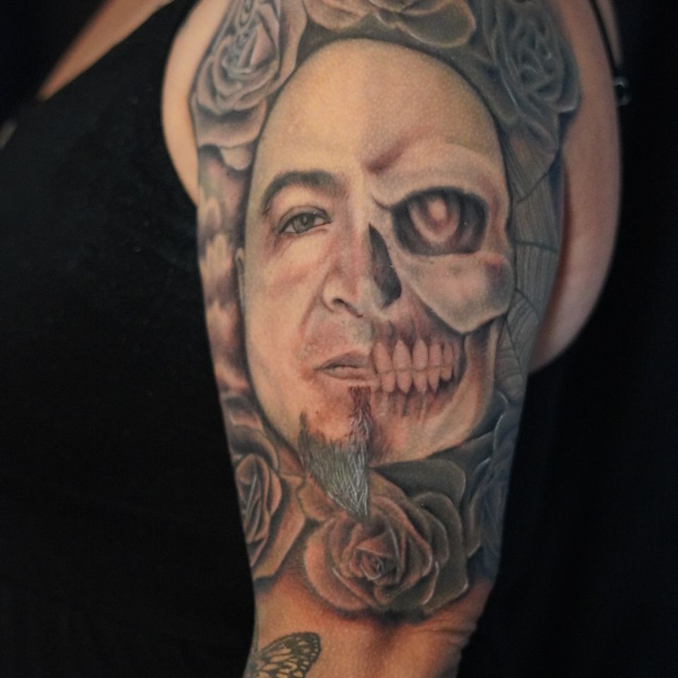 Image of a tattoo showing a half face and half skeleton in great detail surrounded by incredibly detailed flowers