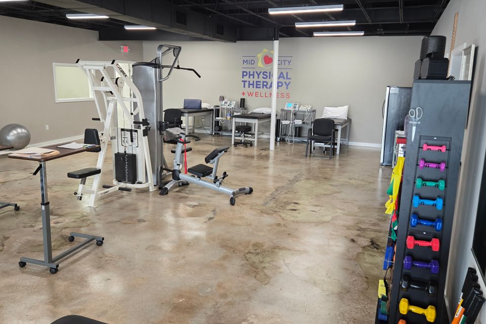 Lat pulldown machine and three open treatment tables in the main therapy area at Mid-City Physical Therapy's Metairie clinic