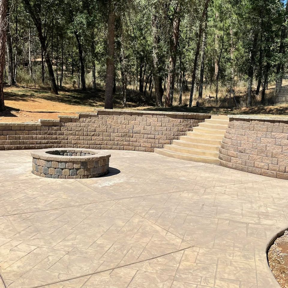 Modern backyard retreat featuring a custom stone fire pit, stamped concrete patio, and a tiered block retaining wall with integrated stairs, professionally designed for outdoor entertainment in Northern California
