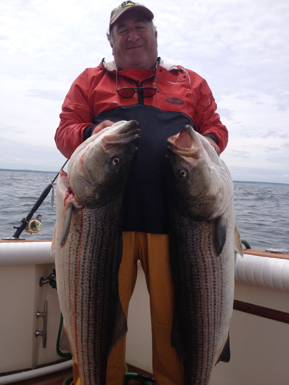 Rob on boat holding 2 huge striped bass