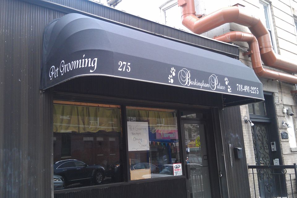 Black storefront awning with white script lettering and a shaped valance on a Brooklyn pet grooming shop