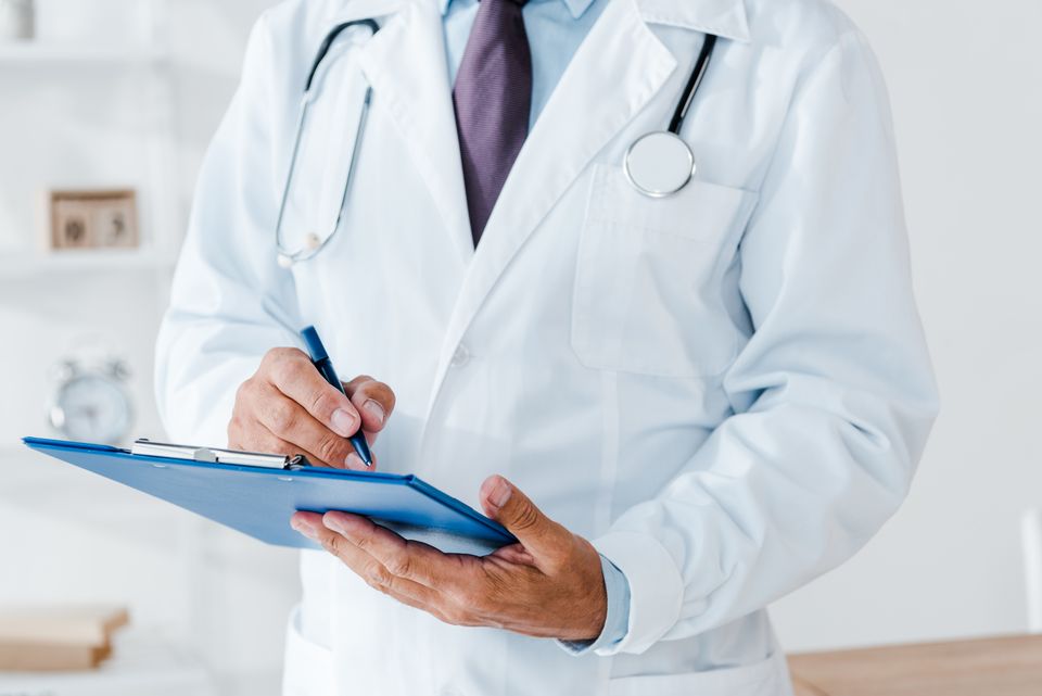 Cropped view of doctor in white coat holding clipboard and writing diagnosis