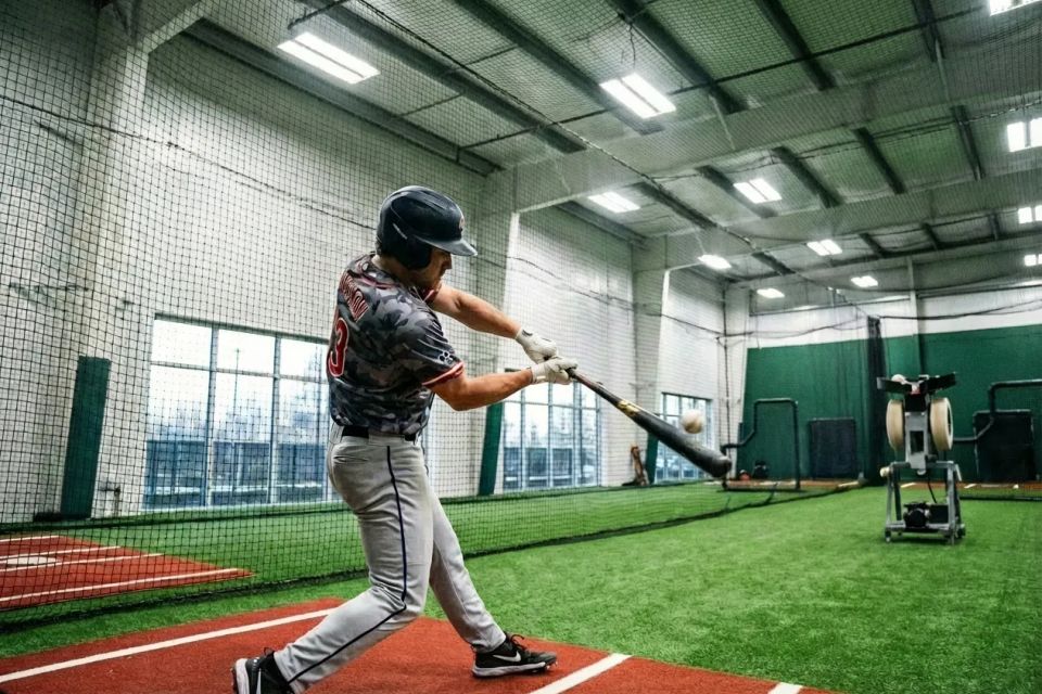  Baseball player hitting ball in indoor batting cage facility with turf floor