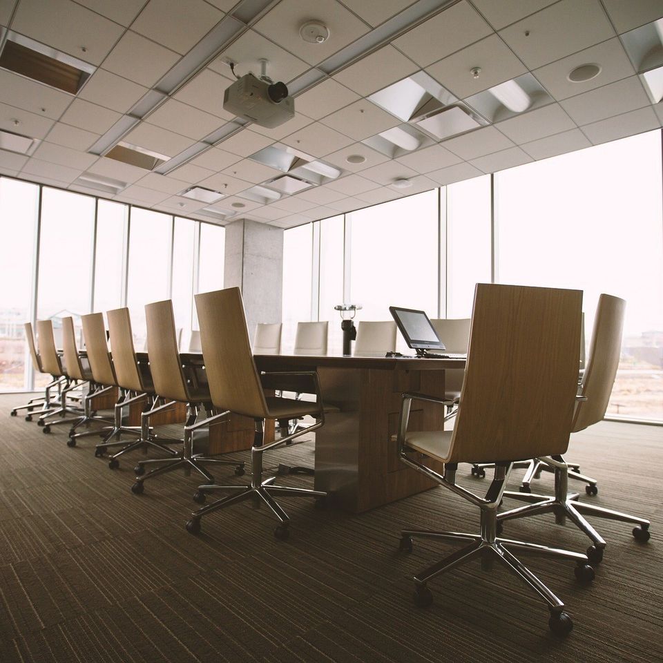 Modern conference room with long wooden table, ergonomic chairs, floor-to-ceiling windows, and presentation equipment