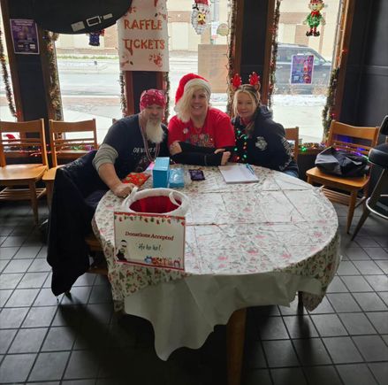 Three volunteers seated at a decorated table during a Christmas-themed fundraising event.