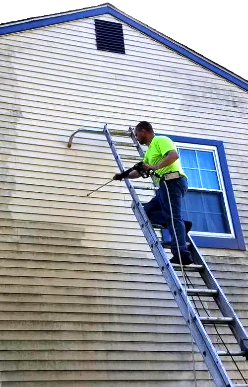 Owner Virgil on a ladder, power washing a house