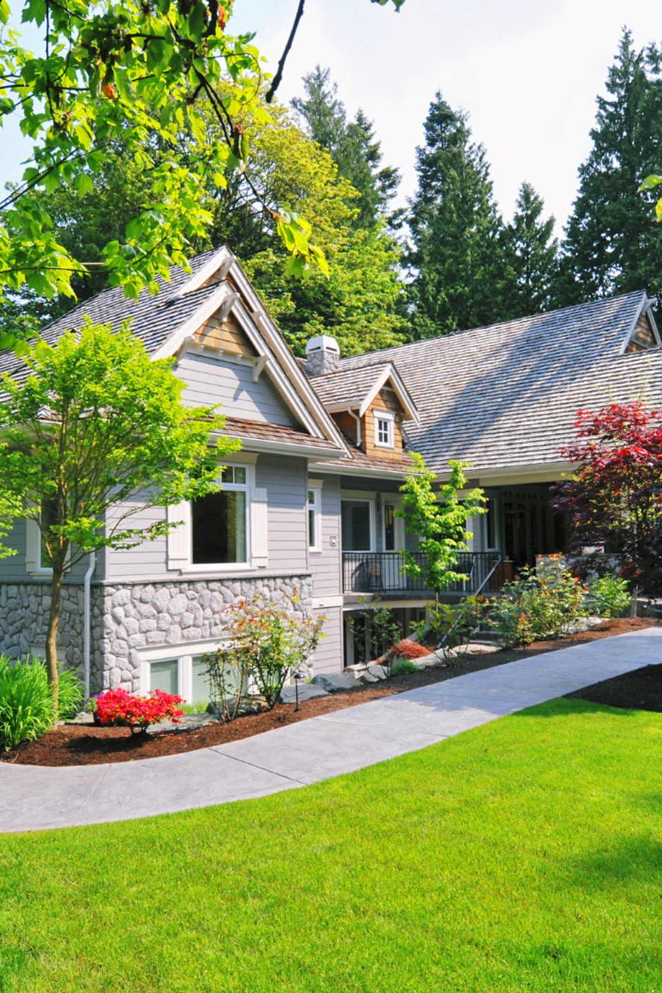 Beautifully landscaped residential property featuring a lush green lawn, colorful trees, flowering plants, mulched garden beds, and a curved walkway.
