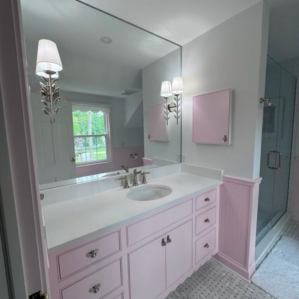 Bathroom remodel with pink vanity, marble basketweave tile floor, and glass shower enclosure