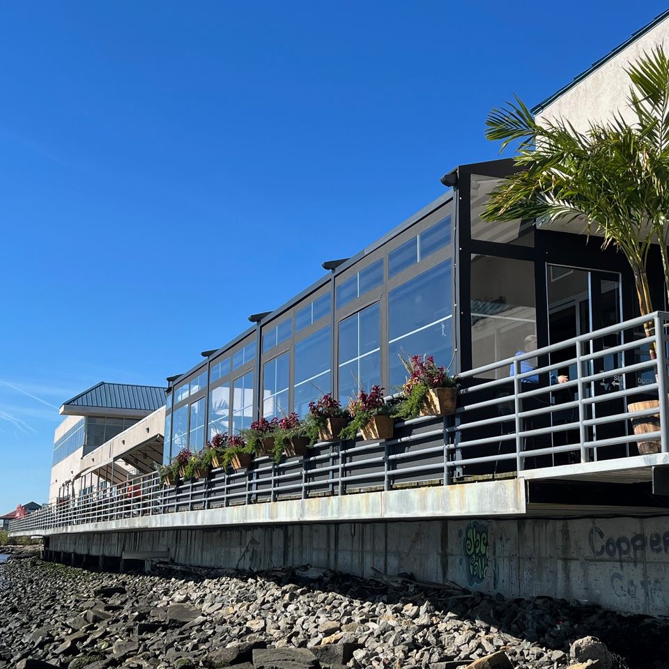 Glass paneled winter enclosure with a black aluminum frame running the length of a waterfront restaurant deck