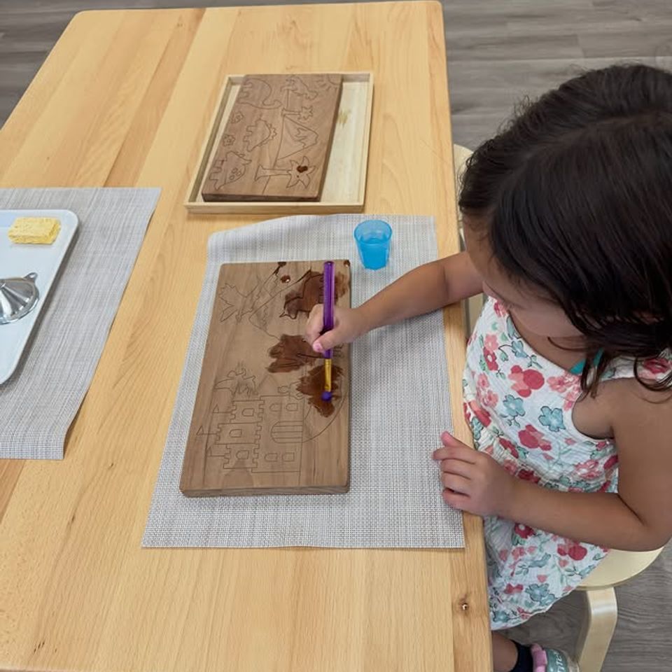 Preschool girl water painting a wooden board during a Montessori art activity in Palmdale CA