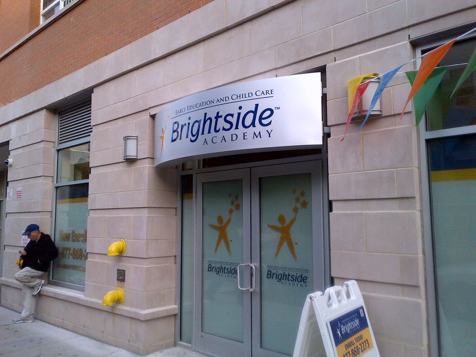 Curved white illuminated cabinet sign with a logo mounted over a double-door entrance