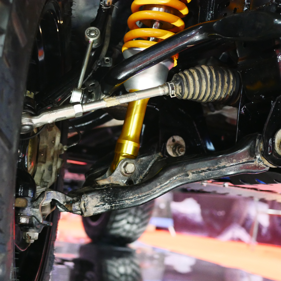 Close-up of a vehicle suspension system featuring a shock absorber, coil spring, and steering components.