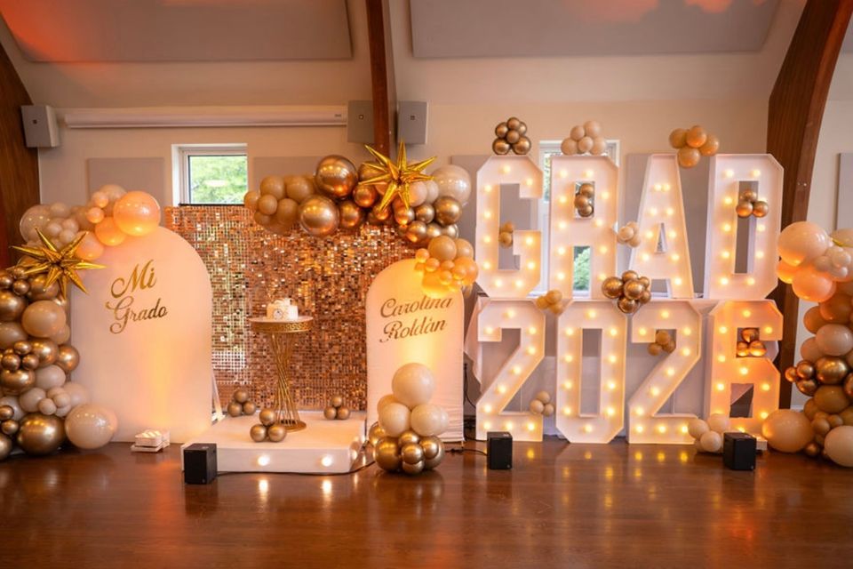 Gold balloon decor, sequin backdrop, and marquee letters styled for a 2026 graduation party