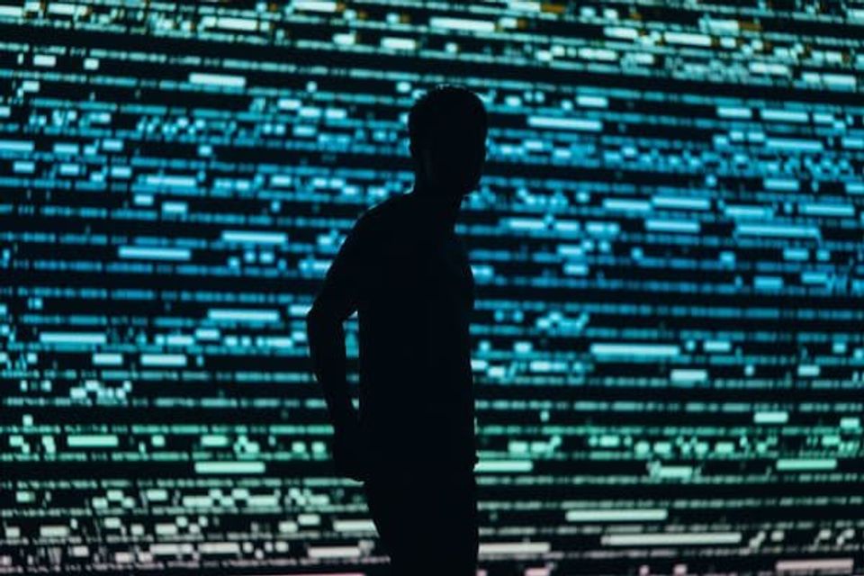 A silhouette of a person behind a screen that looks like the matrix 