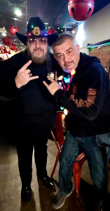 Two guests posing together indoors at a holiday-themed event decorated with festive lights and ornaments.