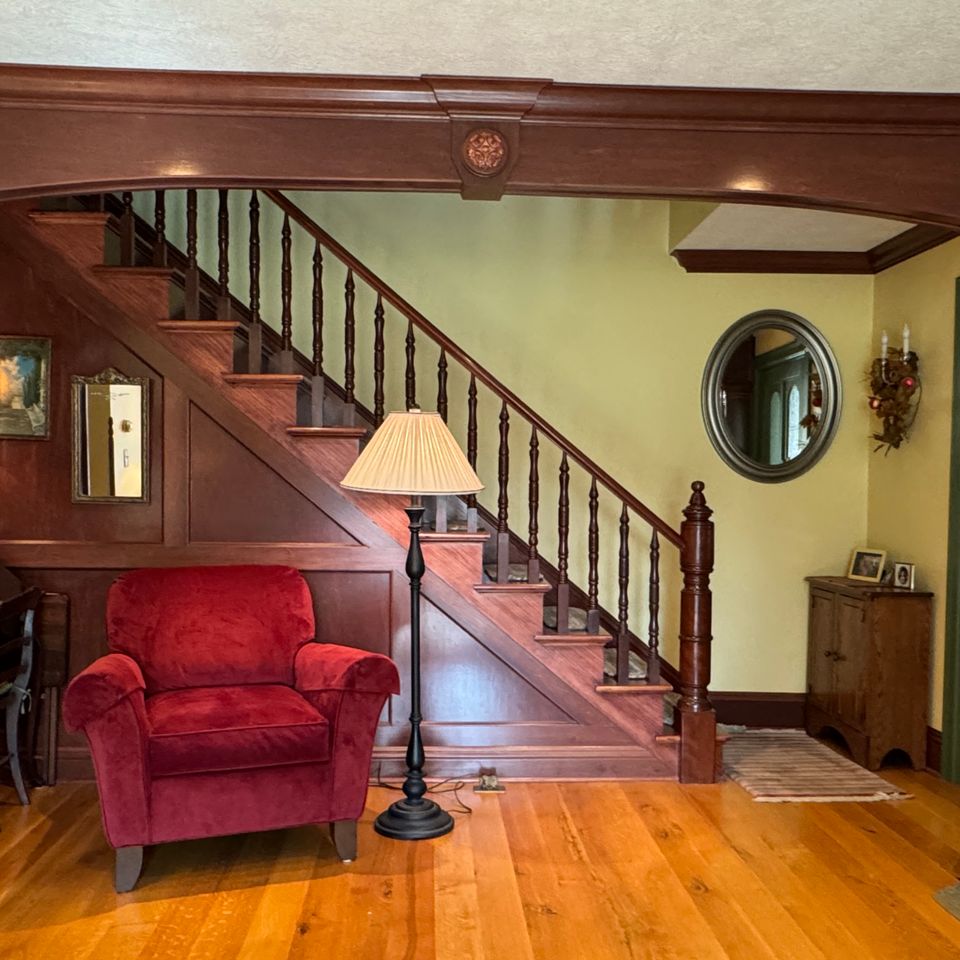 Traditional home interior featuring custom woodwork, a staircase with wood railings, hardwood flooring, and a built-in entryway arch.