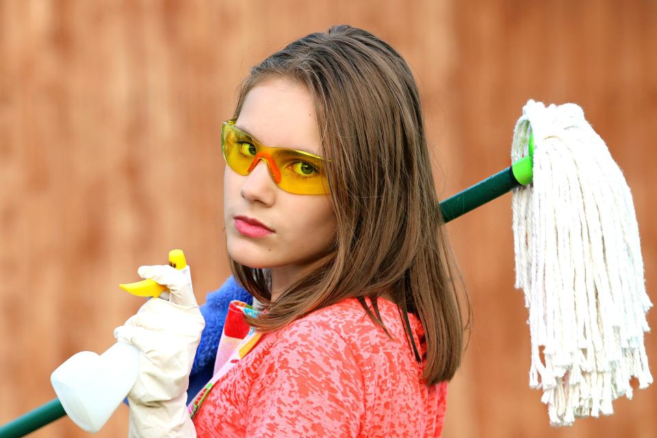 Girl with cleaning supplies and pointing a spray bottle at the camera