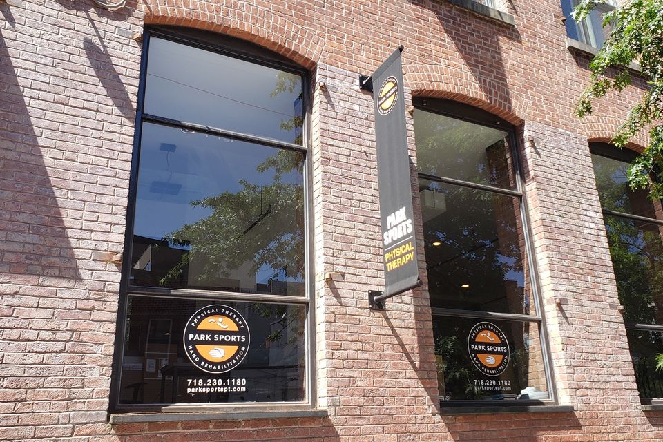 Grey fabric flag sign on a wall bracket beside matching window logos on a brick facade