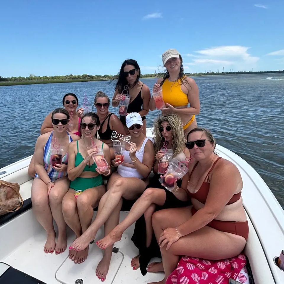 Group of women celebrating a bachelorette party on a Charleston boat tour, holding drinks and smiling at the bow of the boat