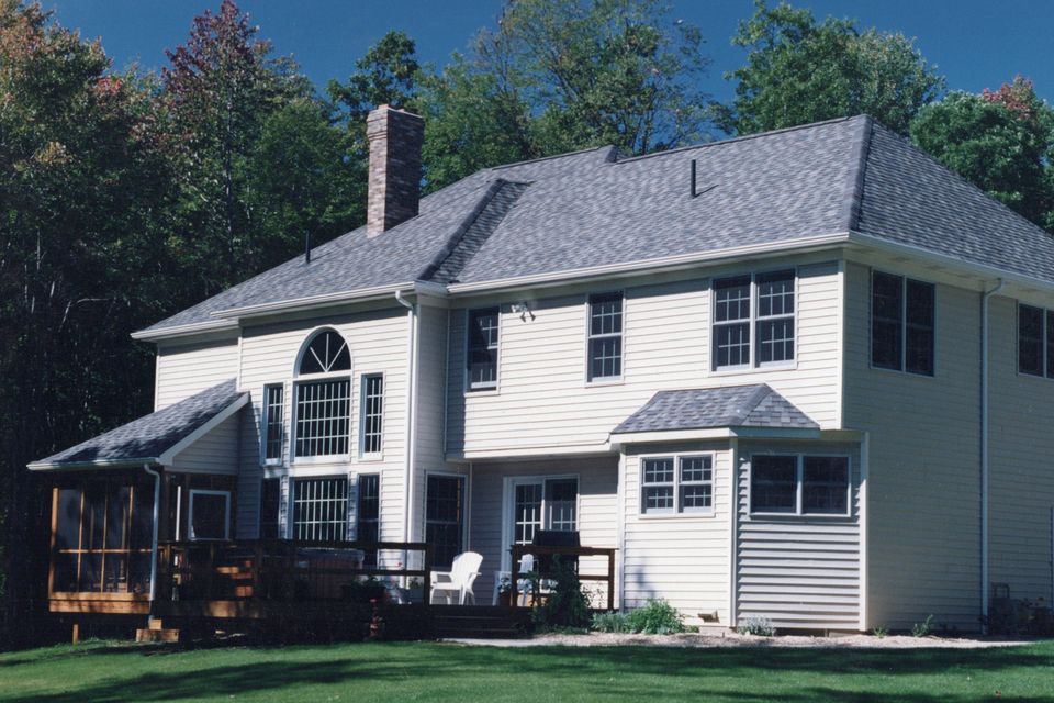 Rear view of a two-story custom home featuring a completed addition, large windows, a deck, and a spacious backyard.