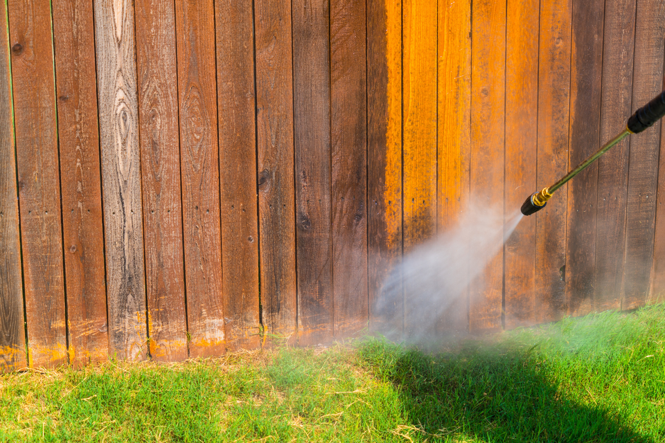 Pressure washing a wooden fence to remove dirt, algae, and weather-related buildup from the surface.