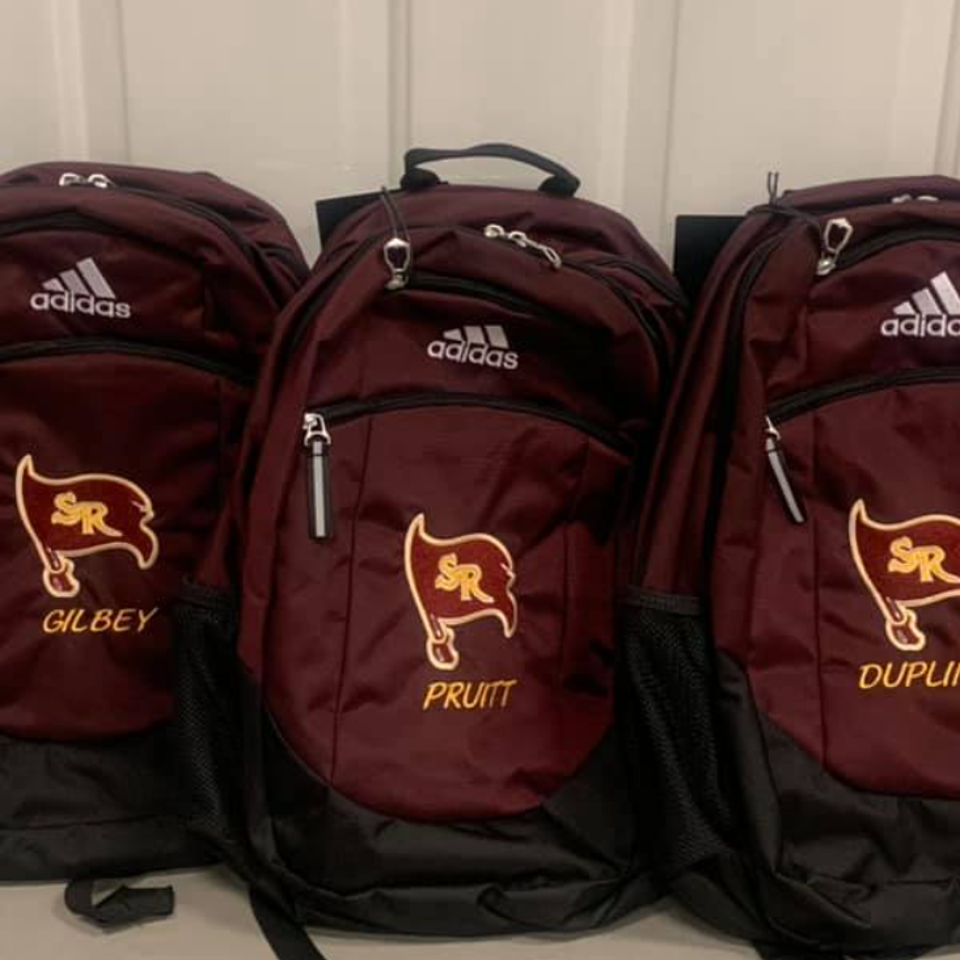 Three maroon Adidas backpacks embroidered with the South Range Raiders flag logo and personalized names.
