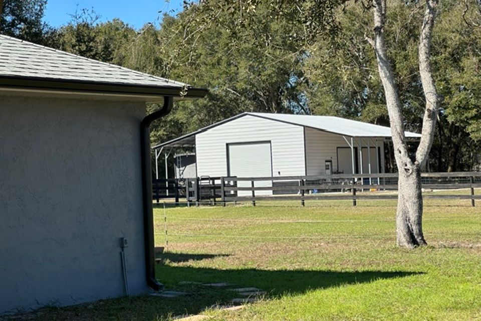 Tan steel barn with covered lean to on fenced rural lot representing steel barns in Alabama