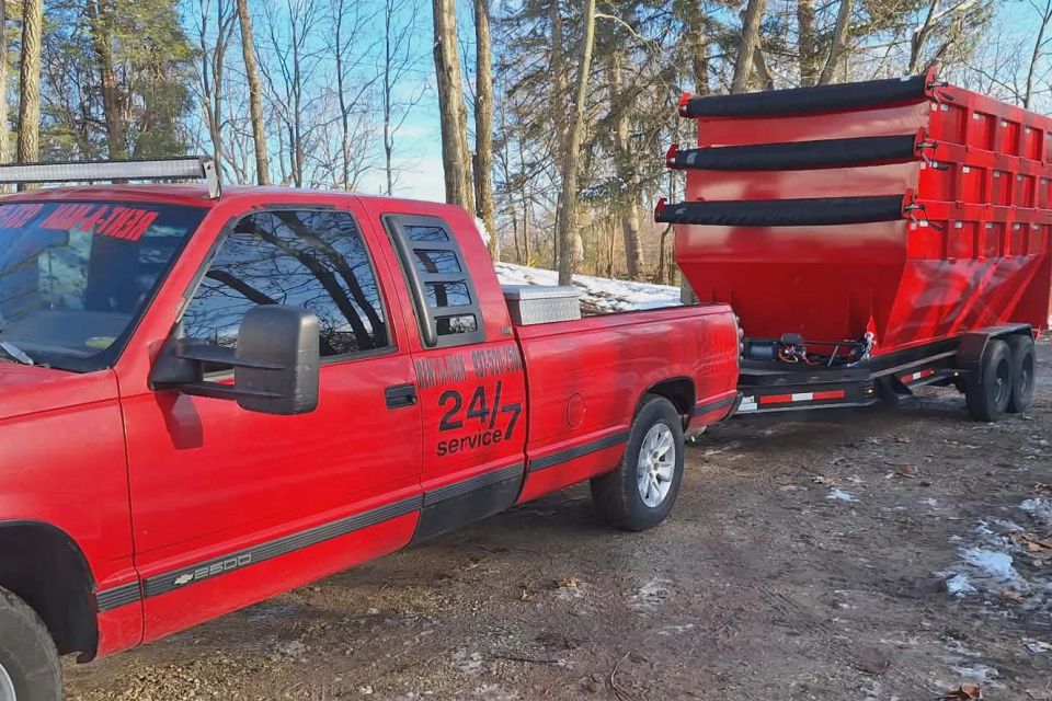 Red Rent-A-Man Dumpster Rentals truck towing a large red roll-off dumpster.
