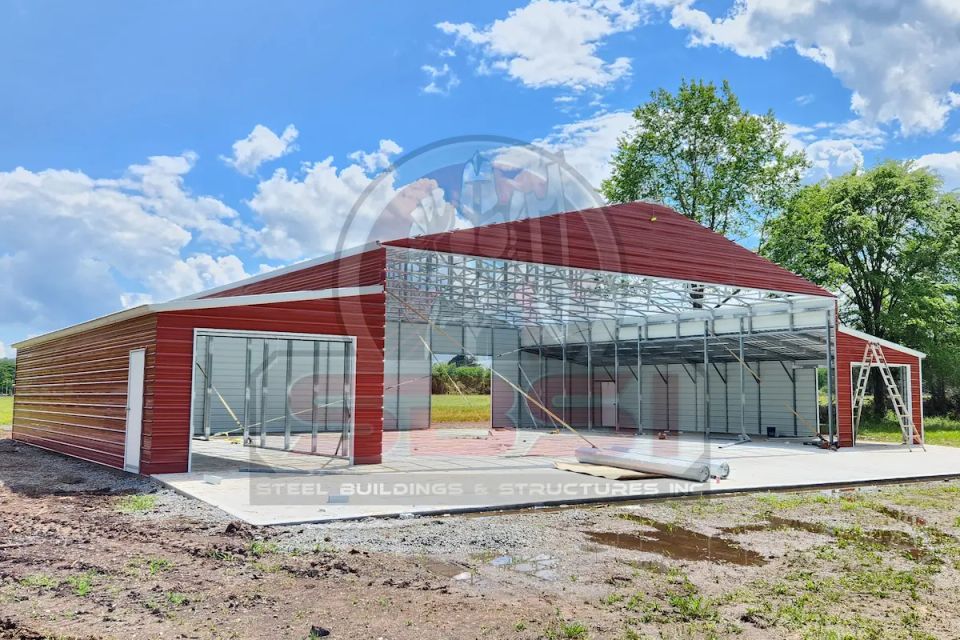 Red and tan steel barn with open framing under construction with SBSI watermark representing steel barns in Alabama