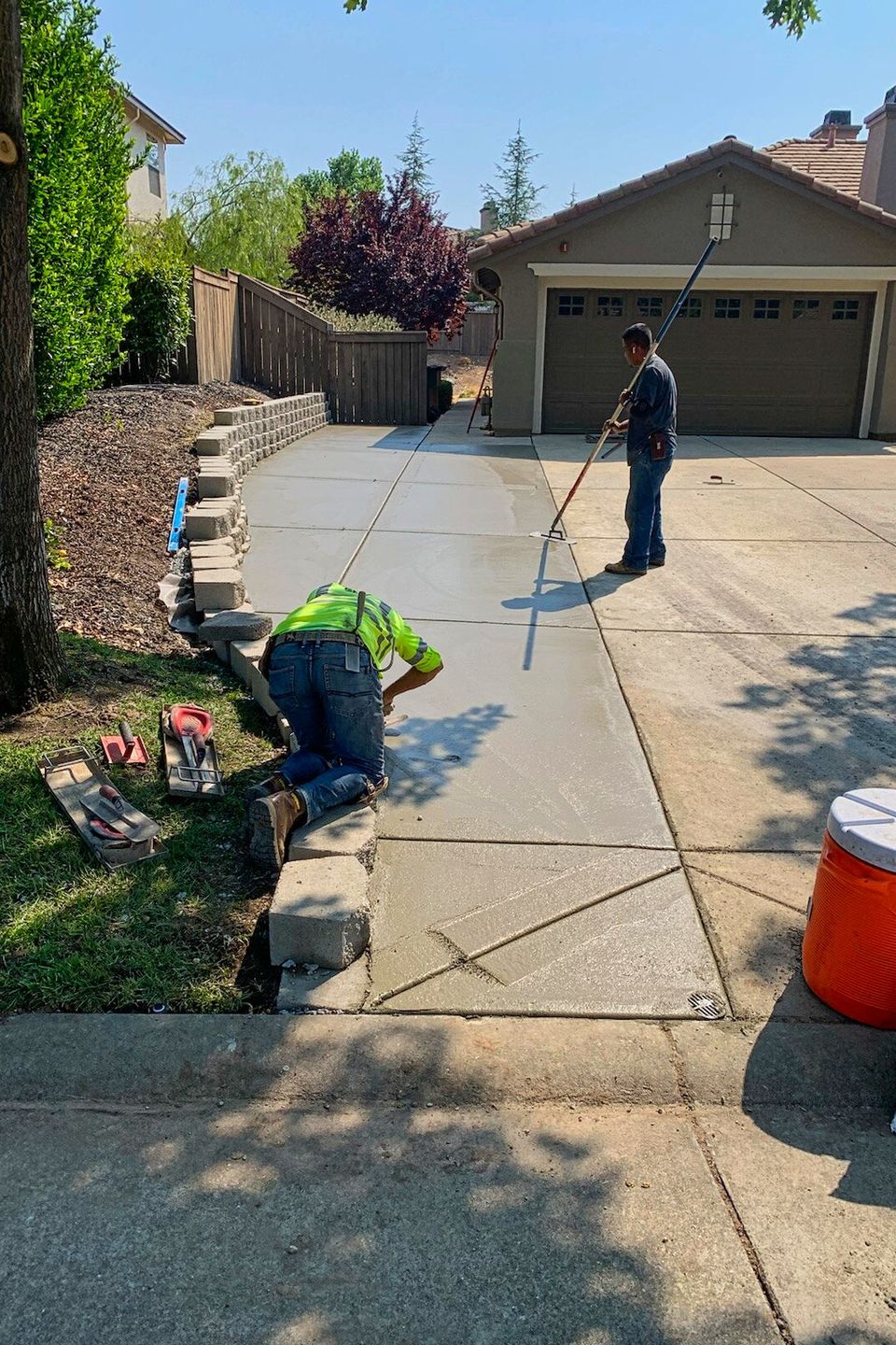 Professional paving crew from Alta Vista Landscaping & Tree Service finishing a custom concrete driveway extension with precision leveling and integrated stone retaining wall