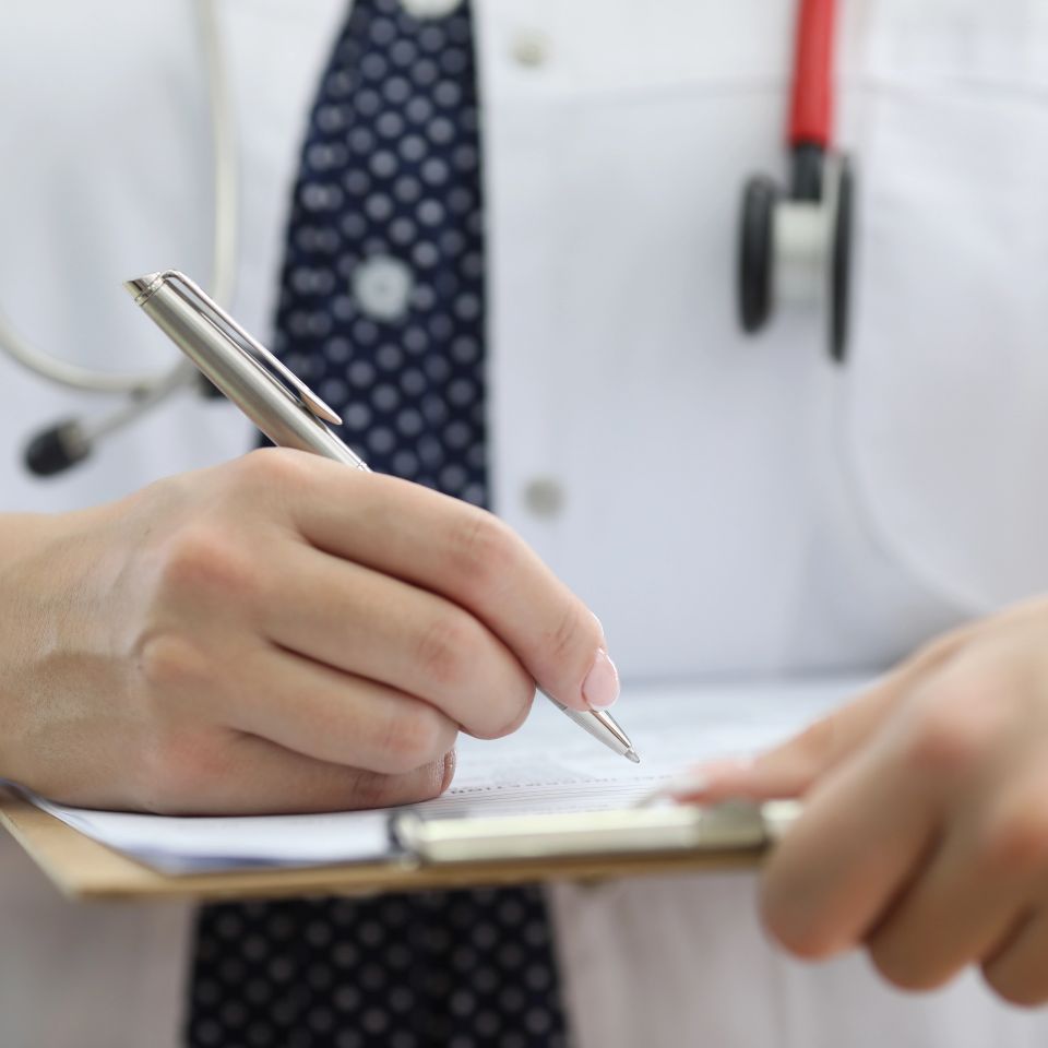 Close-up of doctors hand filling out patients' symptoms on a clipboard