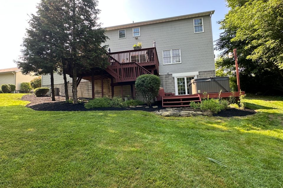 Backyard landscape with a raised deck, hot tub, manicured lawn, mulched planting beds, and trimmed shrubs maintained by R.E.P. Companies.