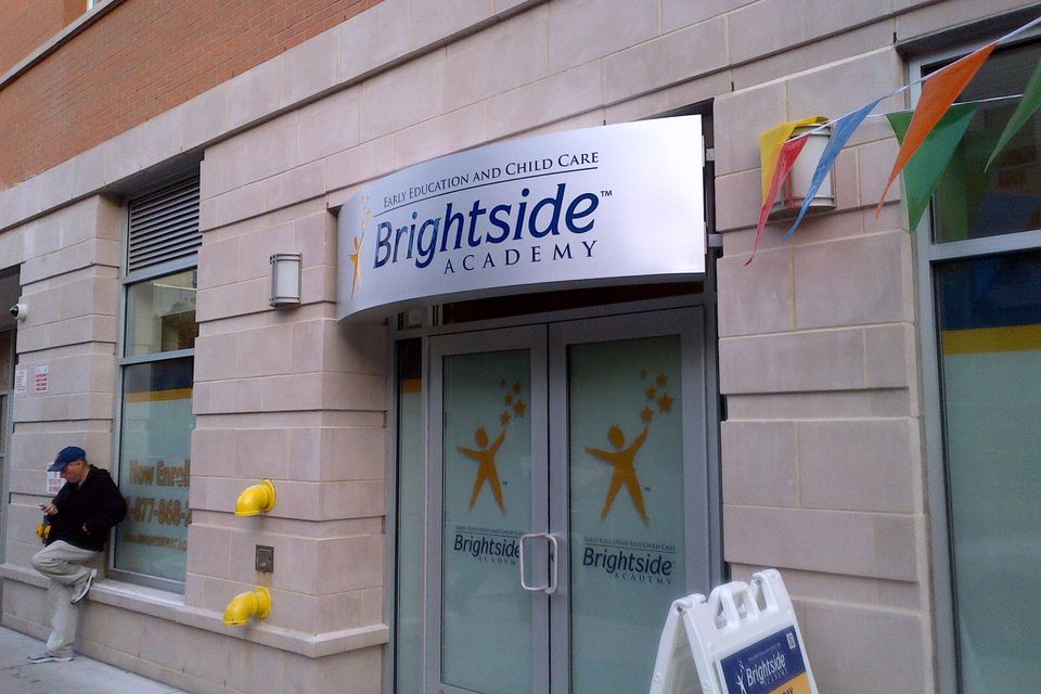 Curved white illuminated cabinet sign with a logo mounted over a double-door entrance